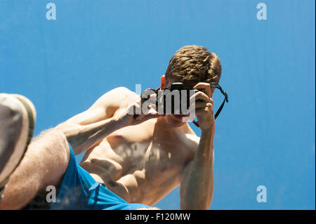 Mais pauvre homme musclé avec son top off prendre des photos de lui-même dans un miroir. Résumé photos. Le miroir est allongé sur l'herbe. Banque D'Images