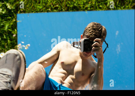 Mais pauvre homme musclé avec son top off prendre des photos de lui-même dans un miroir. Résumé photos. Le miroir est allongé sur l'herbe. Banque D'Images