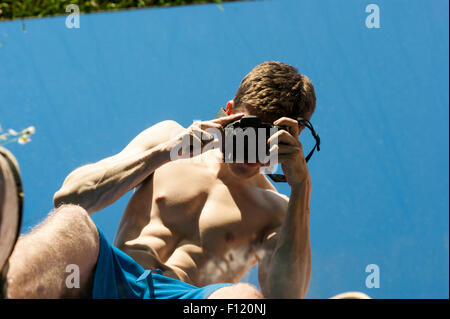 Mais pauvre homme musclé avec son top off prendre des photos de lui-même dans un miroir. Résumé photos. Le miroir est allongé sur l'herbe. Banque D'Images
