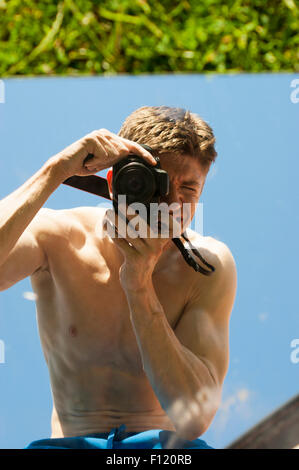 Mais pauvre homme musclé avec son top off prendre des photos de lui-même dans un miroir. Résumé photos. Le miroir est allongé sur l'herbe. Banque D'Images