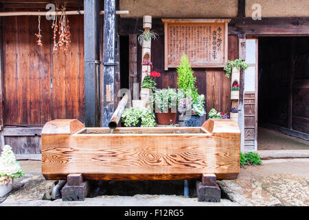 Tsumago, au Japon. Rue de Terashita sur l'ancienne route Nakasendo. Cheval de bois creux avec tuyau d'alimentation. Signer, fleurs et entrée au inn derrière creux. Banque D'Images