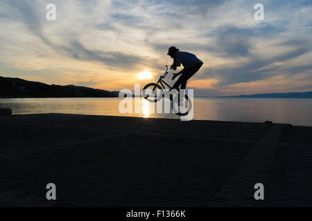 Silhouette biker Bmx faisant des tours contre le coucher du soleil. Banque D'Images