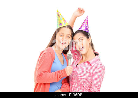 Deux adolescentes avec chapeaux de fête en chantant dans un micro et regardant la caméra isolé sur fond blanc Banque D'Images