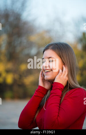 Young woman listening music avec des écouteurs et le chant à l'automne parc, Porter du rouge pull Banque D'Images