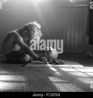 Toddler sitting on floor counting money Banque D'Images