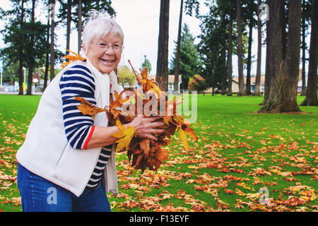 Senior woman holding poignée de feuilles d'automne Banque D'Images