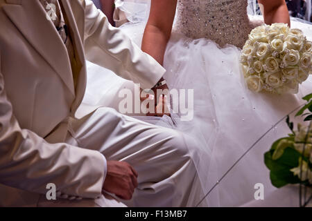 Les mariés se tenant la main à travers le service de mariage. Banque D'Images