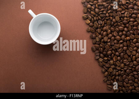 Tasse blanche vide sur fond brun avec les grains de café Banque D'Images