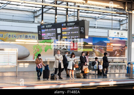 Le Japon. Shin Osaka station. 22 de la plate-forme. Groupe de personnes, certaines avec une assurance d'attendre en file pour le prochain train en vertu d'affichage avec le train d'informations. Banque D'Images