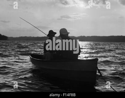 Années 30, deux hommes portant des chapeaux EN ANONYME PÊCHE BARQUES SILHOUETTÉ AU LEVER DU SOLEIL Banque D'Images