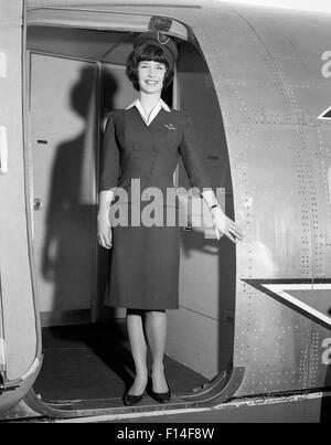 1960 SMILING STEWARDESS STANDING IN DOORWAY OF AIRPLANE LOOKING AT CAMERA Banque D'Images