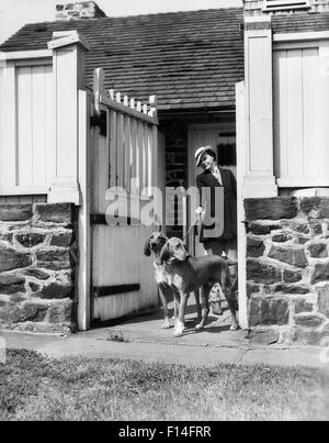 1930 FEMME SPORTIVE HAUT DE GAMME AVEC DEUX FOX HOUND CHIENS EN LAISSE PAR KENNEL GATE Banque D'Images