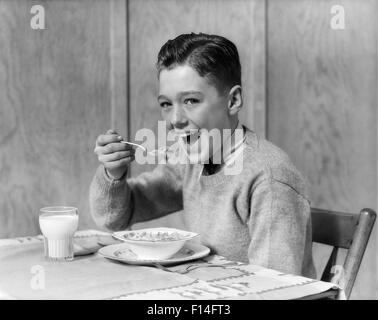 Années 1930 Années 1940 SMILING BOY LOOKING AT CAMERA MANGER LE PETIT DÉJEUNER BOL DE CÉRÉALES ET UN VERRE DE LAIT Banque D'Images