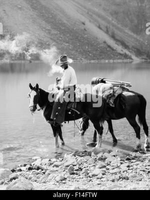 Années 1920 Années 1930 HOMME COWBOY SUR CHEVAL AVEC PACK HORSE PAR MORAINE LAKE ALBERTA CANADA Banque D'Images