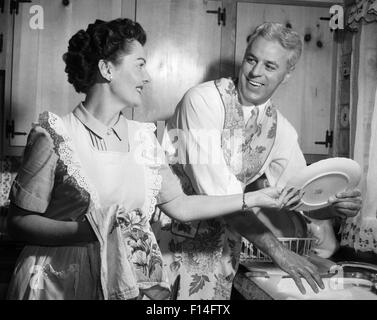 1950 SMILING MARI EN TABLIER DANS LA CUISINE LAVE-VAISSELLE AUSSI HEUREUX FEMME DRIES Banque D'Images