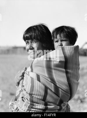 1930 SMILING NATIVE AMERICAN MOTHER LOOKING AT CAMERA EXERÇANT SON BÉBÉ SUR SON DOS COCHITI PUEBLO NOUVEAU MEXIQUE USA Banque D'Images