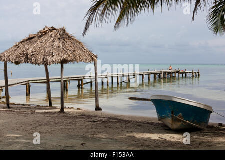 Une scène de plage avec un vieux bateau, une cabane ouverte couverts de chaume, un dock avec soleil touristes et une tempête se déplaçant dans sur les Caraïbes Banque D'Images