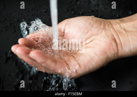Caucasian woman's hand rondelles à l'eau courante avec des bulles et de l'eau pénétrant par les doigts et un fond noir. Banque D'Images