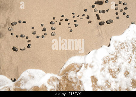 Mot de l'été écrit sur le sable avec des pierres sombres, dans une plage. Idée d'été et de l'atmosphère. Banque D'Images