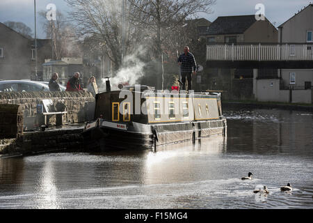 Regardées par les employés, l'homme à l'aide d'un pinceau, est debout sur le toit & lave-amarré canal boat - Leeds Liverpool Canal, Skipton, Yorkshire du nord de l'Angleterre, Royaume-Uni. Banque D'Images