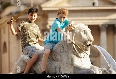 Portrait de deux enfants sur lion statue, Fontaine de l'Obélisque, la Piazza del Popolo (Place du Peuple), l'été, Rome, Latium, Italie Banque D'Images