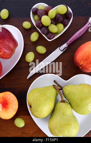 Assortiment de fruits, notamment des pommes, poires, nectarines et les raisins, sur les plaques en forme de coeur blanc sur la table de bois rustique, les frais généraux. Banque D'Images