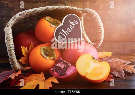 Fruits Fête d'automne de l'action de grâce, avec le kaki et les grenades tumbling d'un panier avec remerciements message sur un bois rustique Banque D'Images