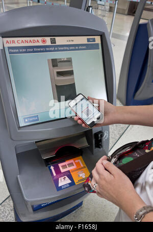 Femme à l'aide de son téléphone mobile et d'accès à bord électronique pour l'enregistrement et obtenir des étiquettes de bagages à l'aéroport de Toronto. Banque D'Images