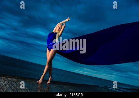 La photographie en extérieur - un grand slim blonde blonde femme fille model posing outdoors sur une soirée humide avec une longue robe fluide bleu flottant dans le vent Banque D'Images