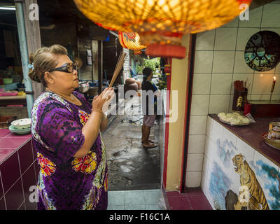 Bangkok, Bangkok, Thaïlande. Août 28, 2015. Une femme prie dans un petit sanctuaire dans le quartier chinois de Bangkok sur l'esprit affamé 24. Les Bouddhistes Mahayana croient que les portes de l'enfer sont ouvertes sur la pleine lune du septième mois lunaire du calendrier chinois, et les esprits des fantômes affamés admis pour parcourir la terre. Ces fantômes ont besoin de nourriture et de mérite à trouver leur chemin de retour à leur propre. Les gens à s'aider en offrant de la nourriture, l'argent en papier, des bougies et des fleurs, ce qui en mérite de leur propre dans le processus. Esprit affamé jour est observé dans les communautés avec une grande population d'origine chinoise comme le Chinatown de Bangkok. (C Banque D'Images