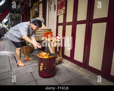 Bangkok, Bangkok, Thaïlande. Août 28, 2015. Une femme burns ''ghost'' de l'argent pour ses ancêtres sur l'esprit affamé dans le quartier chinois de Bangkok de jour. Les Bouddhistes Mahayana croient que les portes de l'enfer sont ouvertes sur la pleine lune du septième mois lunaire du calendrier chinois, et les esprits des fantômes affamés admis pour parcourir la terre. Ces fantômes ont besoin de nourriture et de mérite à trouver leur chemin de retour à leur propre. Les gens à s'aider en offrant de la nourriture, l'argent en papier, des bougies et des fleurs, ce qui en mérite de leur propre dans le processus. Esprit affamé jour est observé dans les communautés avec une grande population d'origine chinoise comme Bangkok Banque D'Images