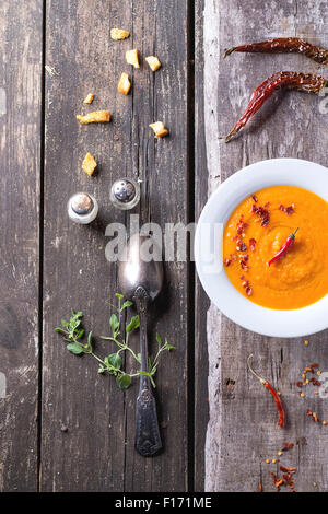 Plaque blanche de soupe crème de carottes avec red hot chili pepper. Plus de vieille table en bois avec vintage cuillère, poivrons, sel et croûtons Banque D'Images