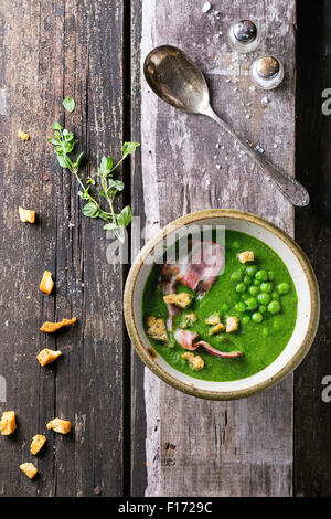 Soupe crème de petits pois dans un bol en céramique avec lard grillé et les croûtons. Plus de vieille table en bois avec vintage cuillère, un grenier à sel Banque D'Images