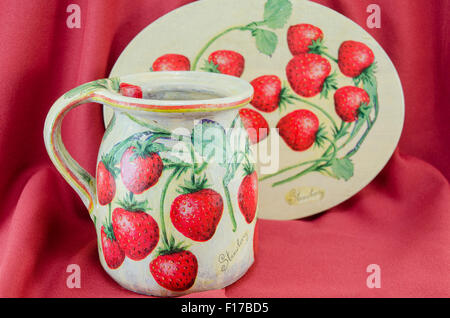 Décoration Découpage motif fraise clay pitcher et Plaque sur fond de tissu rouge Banque D'Images