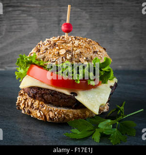 Hamburger gourmet avec fromage suisse et des légumes frais sur pain multigrains sur fond sombre, format carré Banque D'Images
