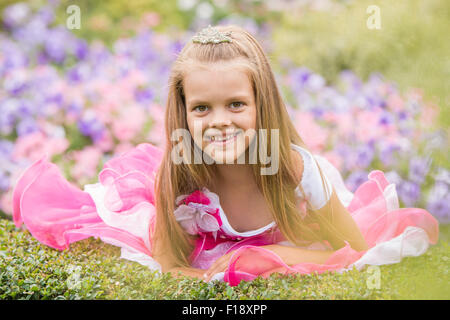 Heureux fillette de six ans dans un cadre de soirée robe rose marche à travers le jardin vert Banque D'Images
