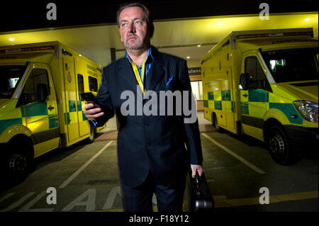 Un mâle en dehors des heures ouvrables, médecin sur appel, tenant un sac de médecine et d'un téléphone mobile, en passant devant une ligne d'ambulances à l'hôpital UK GP Banque D'Images