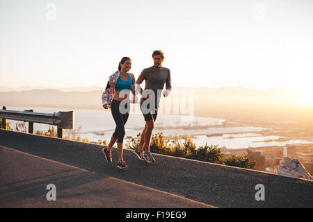 Jeune couple jogging tôt le matin. Jeune homme et femme d'exécution à l'extérieur, sur un coteau road. Banque D'Images