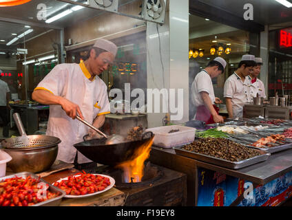 Cuisinier prépare nourriture sur flaming wok au trottoir stand alimentaire dans le quartier musulman de Xi'an, Chine Banque D'Images