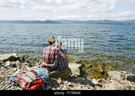 Vue arrière du couple romantique en amoureux embrasser assis au bord de la mer Banque D'Images