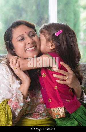 Happy Mother Day. Famille indienne à la maison. Asian girl kissing her mother, assis sur un canapé. Le parent et l'enfant de vie intérieure. Banque D'Images