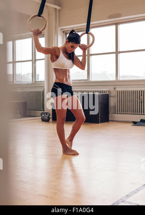 Tourné sur toute la longueur de l'ajustement jeune femme se reposant après l'exercice sur les anneaux de gymnastique. Femme en vêtements sports debout dans une salle de sport holding r Banque D'Images