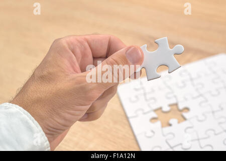 Businessman hand mettant une pièce manquante et résoudre les casse-tête blanche placée sur le dessus de table en bois de chêne, Close up, Banque D'Images