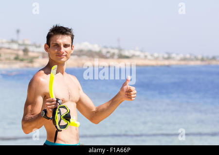 Young smiling man est titulaire d'équipement de plongée avec tuba et montre pouce vers le haut. Vacances d'arrière-plan avec copie espace du côté droit Banque D'Images