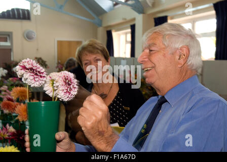 L'évaluation juge mâle une entrée dans une fleur locale show avec une femelle steward regarde sur en arrière-plan, près de Alton, Hampshire, Royaume-Uni. Banque D'Images