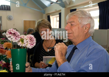 L'évaluation juge mâle une entrée dans une fleur locale show avec une femme à l'intendance sur en arrière-plan, près de Alton, Hampshire, Royaume-Uni. Banque D'Images