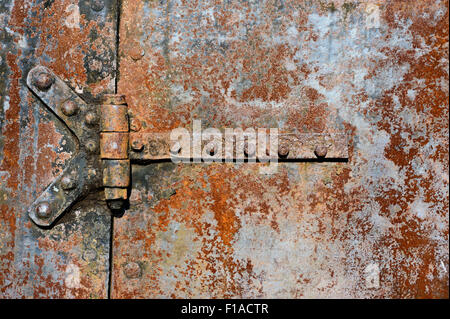 Milieux et de textures : rusty metal surface de la porte avec charnières rivetées, industriel abstract Banque D'Images