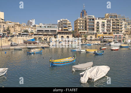 Les bateaux de pêche traditionnels peints dans des couleurs vives avec des bâtiments en pierre au-delà, St Julian's Bay (Malte). Banque D'Images