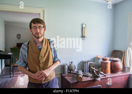 Old Bethpage, New York, USA. 30 août, 2015. Matt, un membre du personnel saisonnier portant des vêtements américains de style traditionnel, donne un tour de la Powell House durant l'ancien temps Music Week-end à Old Bethpage Village Restauration. Un ancien charcutier est sur le coin de l'armoire à côté de lui. La maison a été construite en 1750 et est restauré à sa taille, et élargi 1855 est le seul immeuble de standing sur son emplacement d'origine dans le village. Credit : Ann E Parry/Alamy Live News Banque D'Images