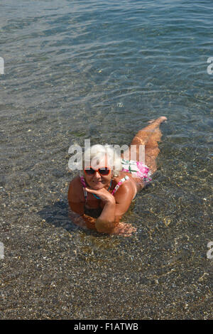 Portrait de senior lady c'est couché dans l'eau peu profonde de la mer de galets de plage. Banque D'Images